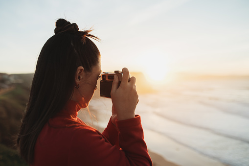 A young woman taking a picture with a camera at sunset