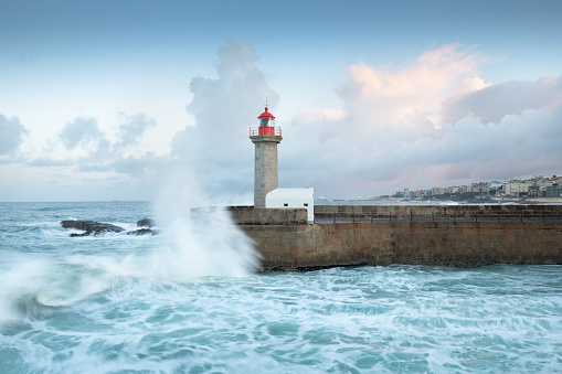 Beautiful sunset on the old pier and The Felgueiras Lighthouse at the mouth of the river Douro, Porto, Portugal\nBig breaking sea wave splash at sunset.