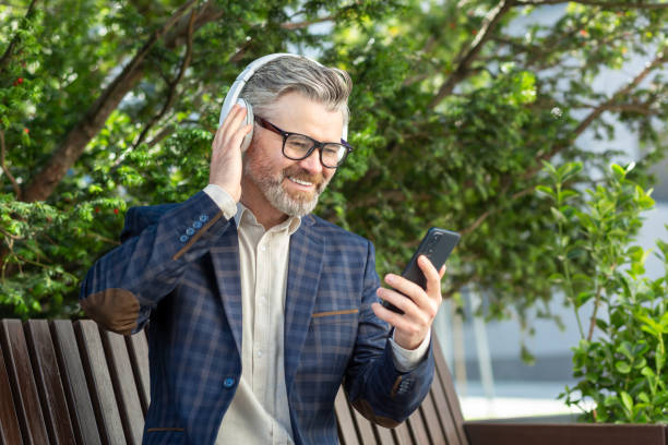 profesjonalny starszy biznesmen cieszący się muzyką na słuchawkach na świeżym powietrzu - office park audio zdjęcia i obrazy z banku zdjęć