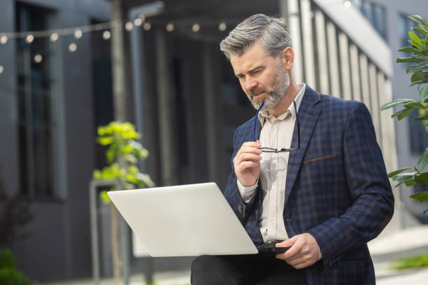 istock Senior businessman analyzing data on laptop outside modern office building 1960610655
