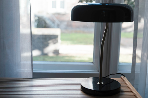 Empty working table with black table lamp in front of window in living room.