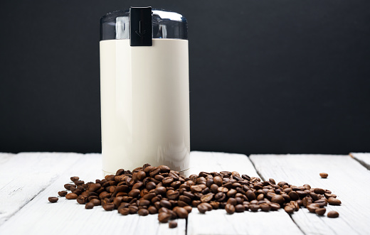 White electric coffee grinder with coffee beans on a white background.