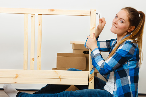 Woman assembling wooden furniture using hex key. DIY enthusiast. Young girl doing home improvement.