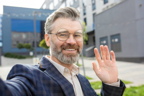 istock Confident senior businessman waving friendly outside modern office building 1960658908
