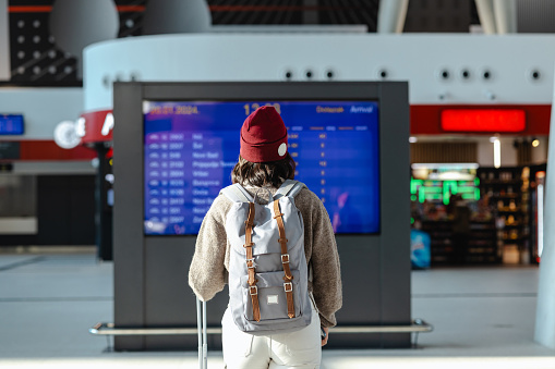 Rear view of young woman standing in front of big arrival departure display on station
