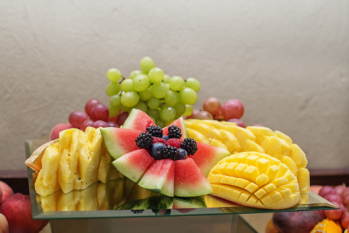 Eating at the event. An artistic display of fresh watermelon, pineapple, grapes, and berries on glass platter for catering event.