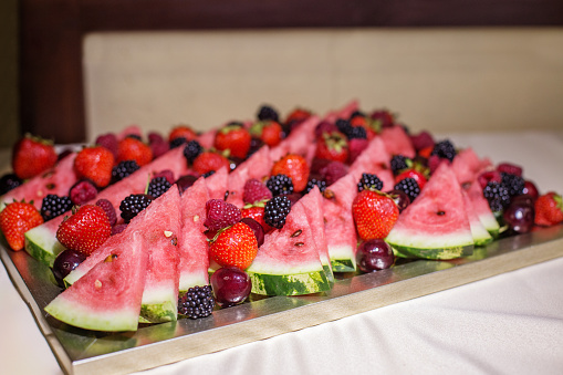 Eating at the event. Vibrant platter of watermelon slices and mixed berries, beautifully arranged for a refreshing summer event or celebration.