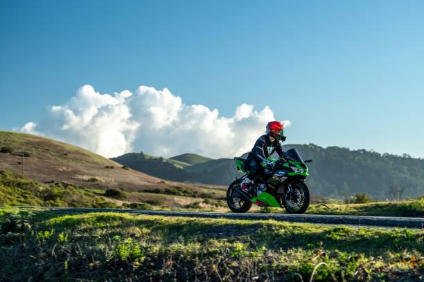 moto solitaire roulant le long d’une crête de montagne avec des paysages spectaculaires et des nuages - motorcycle road journey travel photos et images de collection
