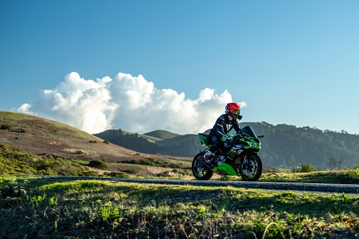 Woodside, United States – January 01, 2024: a Lone motorcycle riding along a mountain ridge with spectacular landscape and clouds in the background