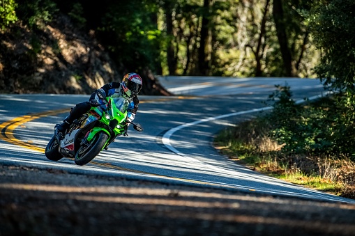 La Honda, United States – December 17, 2023: A Sportbike motorcycle riding through some turns and leaning left with trees and filtered light in the background