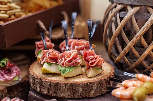Sliced pear and prosciutto canapÃ©s with fresh mint, elegantly presented on rustic wooden log.