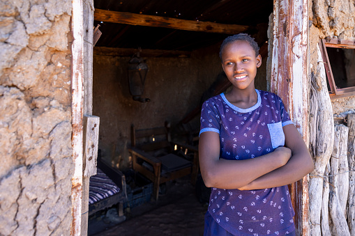 young african girl standing in the empty door frame of her shack, old furniture inside, village in Botswana