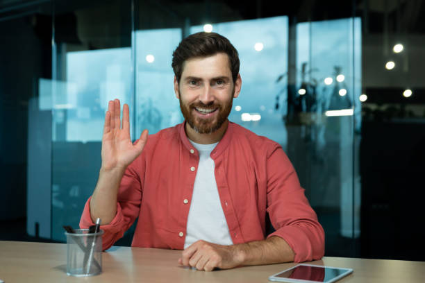 istock Video call, joyful smiling man waving hand greeting gesture working in evening time inside office, web camera view, online meeting with colleagues partners remotely 1960755942