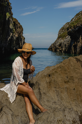 Beautiful young Latin woman, poses on a paradisiacal beach, wearing a white blouse and a straw hat