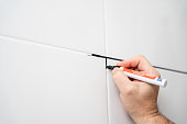 Male hand paints grout on tile joints with a black acrylic marker, home improvement