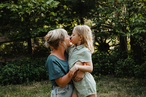 A beautiful mom hugging her eight year old daughter outside. The little girl playfully licks her mom.