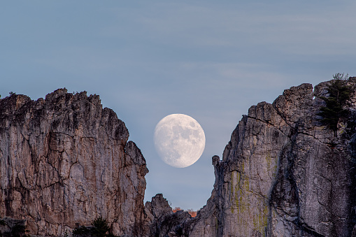 A near full moon rises through the Gun Sight notch above the quartzite fins of Seneca Rocks in West Virginia.