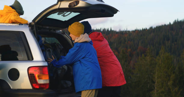 A woman shuts the car trunk after loading it with bags. Pile of snow on the ground. Sunny.