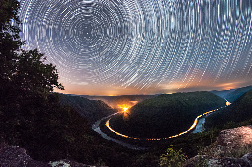 Time lapse of the stars as seen from the main overlook of the New River Gorge in Grandview, West Virginia at night.  A train passing through highlights the bend of the river as it curves through the mountains.