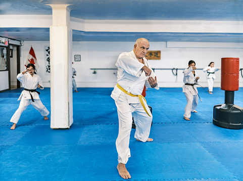 Karate fighter, mature man practising karate with all ages fighters. He is dressed in karategi-karate uniform. Interior of karate school in Mississauga, Ontario in Canada.