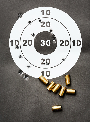 Paper target peppered with bullet holes, with a group of fired, expended cartridge cases in .380 ACP (9mm kurz).