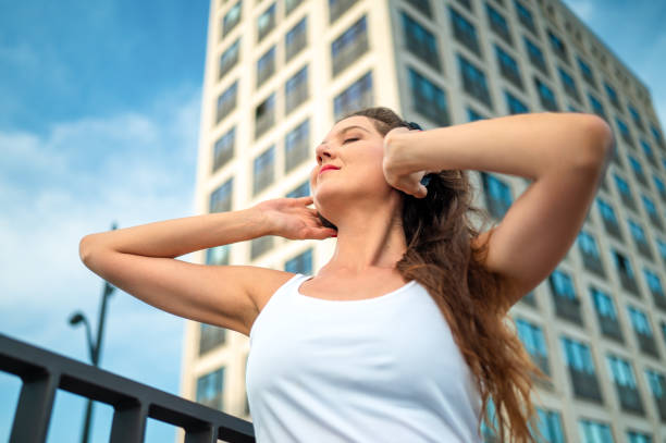 Medium shot of a young caucasian woman against a skycraper listening to music on headphones Low angle perspective of an attractive young woman in a white tank top against a skycraper listening to music on headphones low viewing point stock pictures, royalty-free photos & images