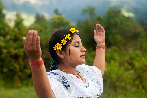 This image captures a moment of cultural significance, showcasing a young indigenous woman adorned with yellow flowers, engaged in a traditional dance amidst the lush greenery of rural Ecuador.