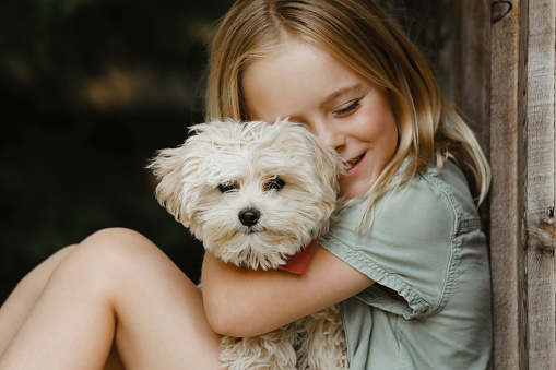A little girl, eight years old, smiles as she hugs her puppy. Sharpest focus on puppy.