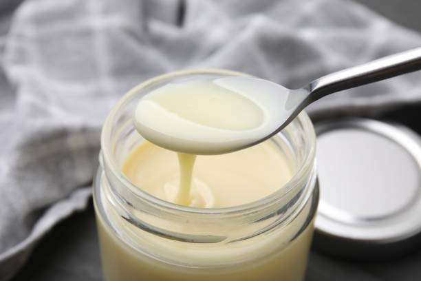istock Condensed milk flowing down from spoon into jar on table, closeup 1960983603