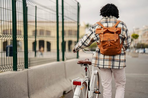 Rear view of a hipster pushing a bicycle while walking on a Europe city street.