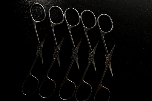 Five new silver sharp manicure scissors close-up lie open on a surface with a black background, cut cuticles