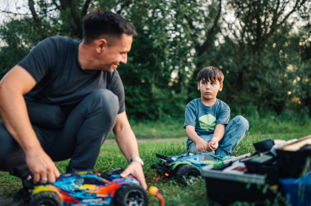 istock Father smiling at son while fixing toy cars in nature. 1961054473