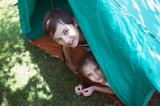 Two happy hiker kids having fun in a tent. Friends, joy, togetherness, play outside, healthy lifestyle.