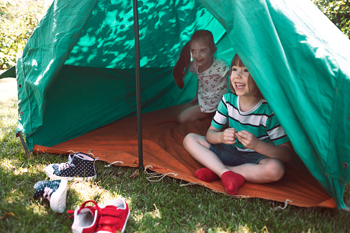Two happy hiker kids having fun in a tent. Friends, joy, togetherness, play outside, healthy lifestyle.