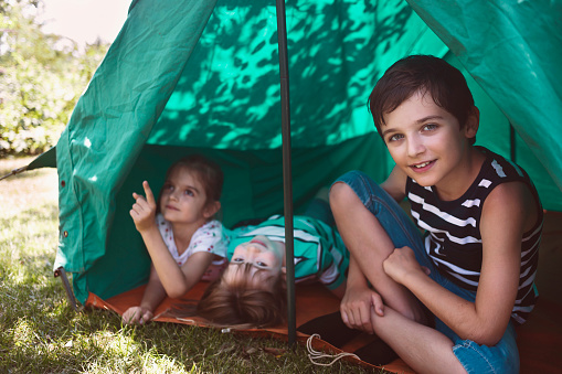 Three happy hiker kids having fun in a tent.