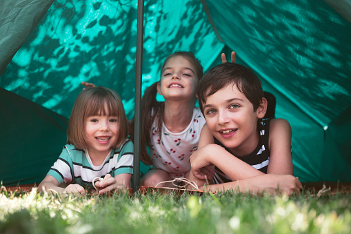 Three happy hiker kids having fun in a tent.