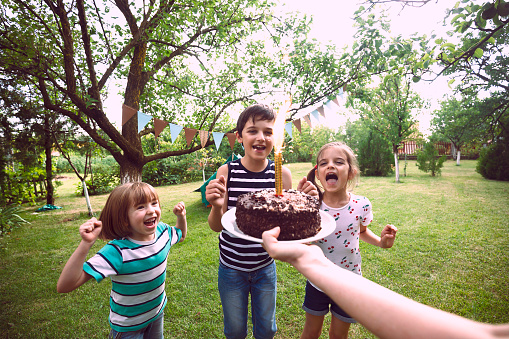 Smiling  children celebrating birthday party in the backyard. Mother's personal perspective.