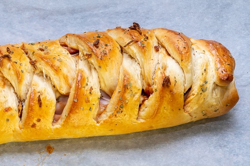 Pizza braid. Delicious braided pizza bread stuffed with cheese, bacon, ham and tomato or barbecue sauce on white baking paper. Horizontal photo and selective focus.