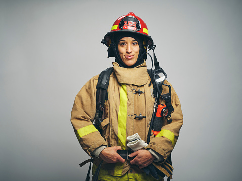 A studio portrait of a female firefighter against a gray background.