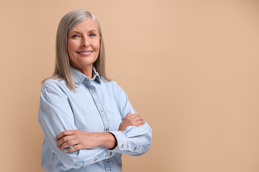 Portrait of beautiful middle aged woman on beige background, space for text