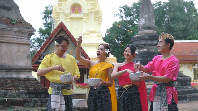 Happy group of young people dressed in traditional Thai clothing are playing in the water during the Thai Songkran festival.