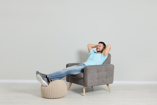 Happy man sitting in armchair near light gray wall indoors