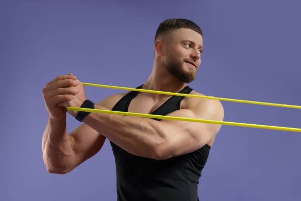 istock Muscular man exercising with elastic resistance band on purple background 1961175646