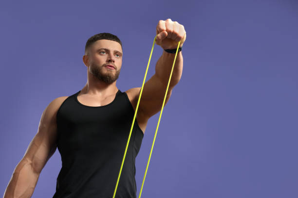 istock Muscular man exercising with elastic resistance band on purple background, low angle view. Space for text 1961175664