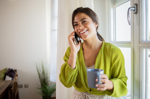 A happy entrepreneur having a phone call in kitchen at her home.