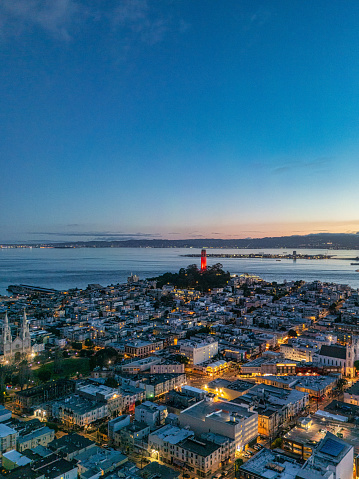 Aerial view at sunrise looking across North Beach at an illuminated Coit Tower colored red.