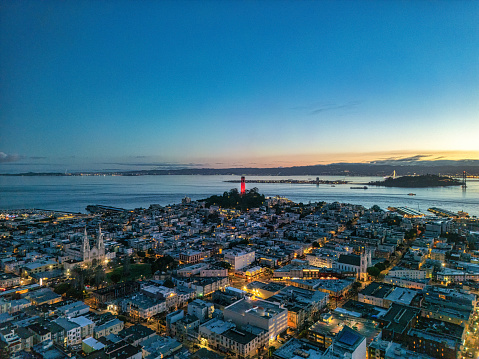 Aerial view at sunrise looking across North Beach at an illuminated Coit Tower colored red.