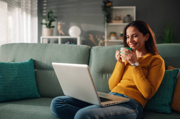 istock Woman using laptop while sitting on couch at home and drinking tea 1961353345