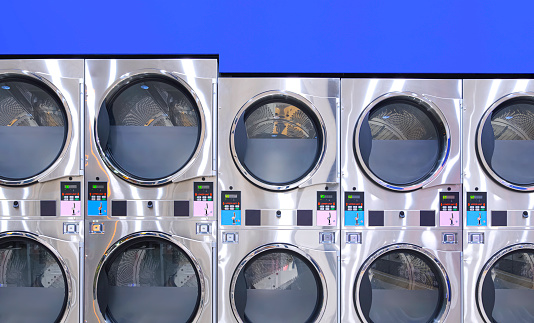 Rows of Vending Washing Machines and Clothes Dryer on blue wall background  in modern Laundromat Shop are opening to service general customers