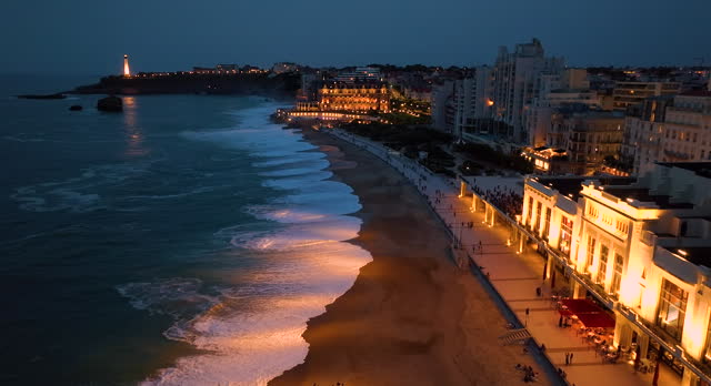 Aerial view incredibly beautiful view of the city of Biarritz at night. Ocean waves illuminated by night lights wash the beaches of the night tourist city. France